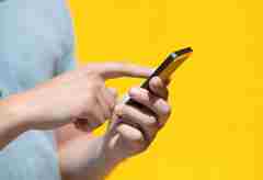 A person using her mobile phone against a yellow background. 