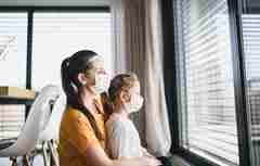 A mother and child with face masks looking through window